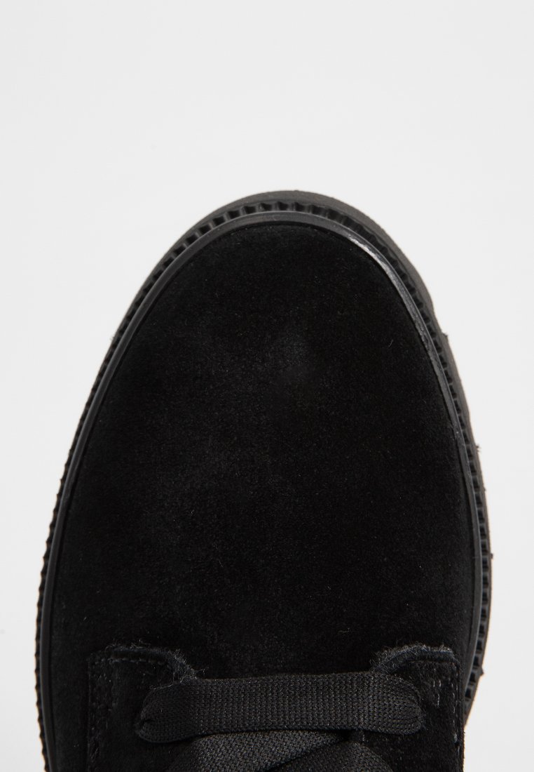 Zwarte suedestal met een ronde neus, gemêleerde bovenkant, platte veters en een rubberen zool met een verhoogde randafwerking.