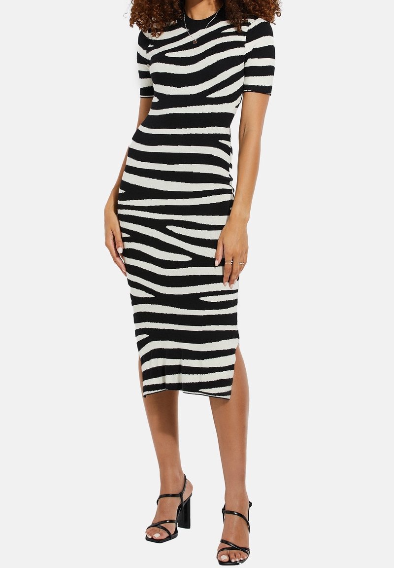 Robe noire et crème à rayures, longueur genou, avec des manches courtes, à la coupe ajustée et une fente sur le côté. Tissu tricoté lisse avec une texture subtile.