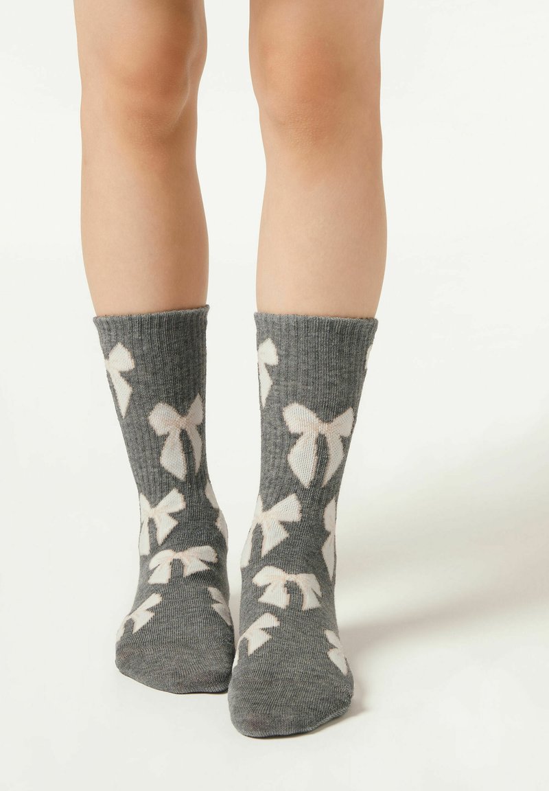 Graue Stricksocken mit weißen Schleifenmustern, ausgestattet mit gerippter Struktur und umgeschlagenem Bündchen, geeignet für die Freizeit.