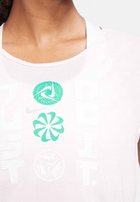 Light pink Nike t-shirt with a round neck. Features green logos and text: "JUST DO IT" in a bold, modern font. Soft, smooth fabric.
