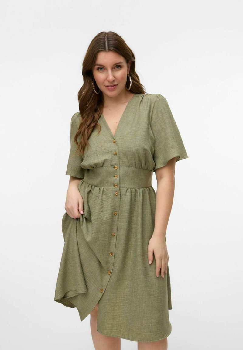 Grøn knap-front kjole med korte ærmer og bælte i taljen. Stoffet har en textured overflade og falder til midt-klasse længde.