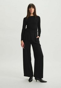 Haut noir à manches longues associé à un pantalon noir taille haute à jambes larges. Le matériau semble lisse ; le pantalon présente des plis à l'avant et une ceinture.