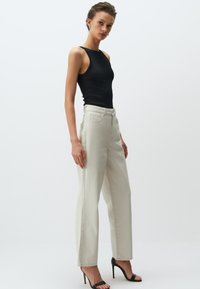 Zwarte geribbelde tanktop gecombineerd met lichtbeige hoge taille wijde broek. Model draagt zwarte stiletto hakken.
