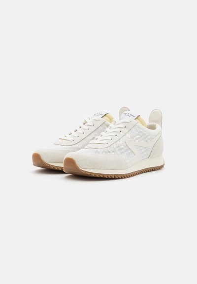 White sneakers with mesh and suede panels, cream accents, round laces, and a textured rubber sole featuring zigzag patterns.