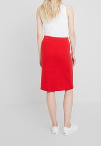 Rode geribbelde gebreide midi rok met een aansluitende tailleband, gecombineerd met witte instappers. Gladde textuur en aansluitend ontwerp.