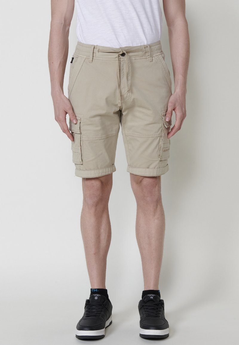 Shorts cargo bej cu multiple buzunare laterale, talie cu șnur și o croială lejeră, fabricate dintr-un material din bumbac cu o textură fină.