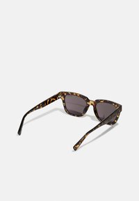 Brune skjoldbrille med katteøyeform. Mørke linser og brede plastikkrammer har et subtilt mønster og en glatt tekstur.