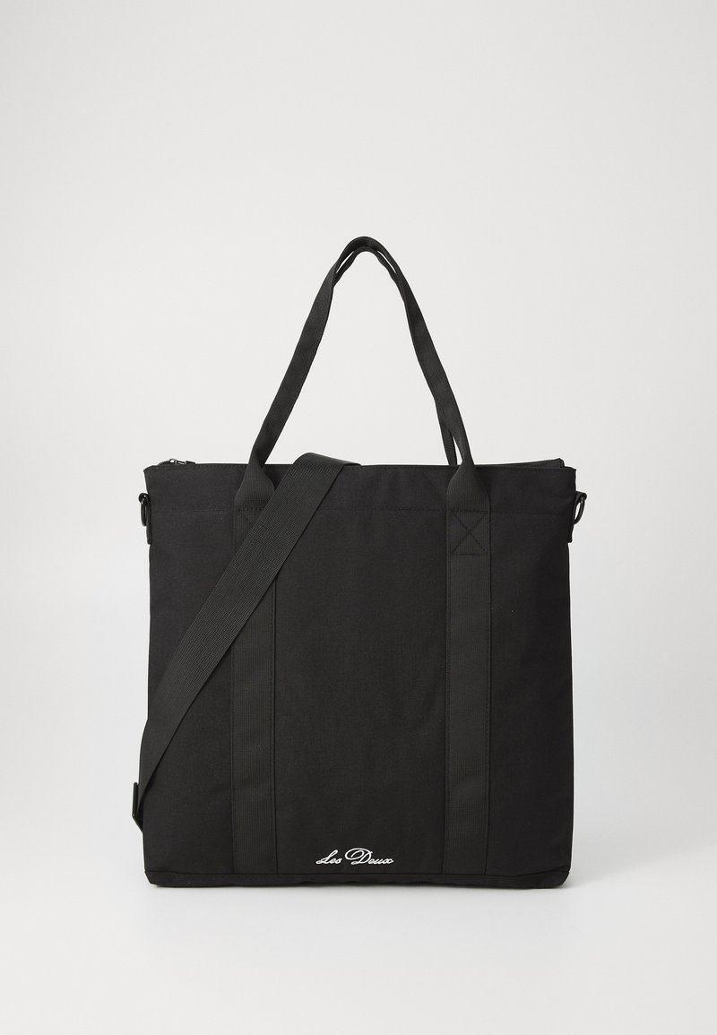 Μαύρη τσάντα tote φτιαγμένη από ανθεκτικό ύφασμα με δύο επάνω χερούλια και αποσπώμενη ιμάντα ώμου. Διαθέτει κλείσιμο με φερμουάρ και πλευρικά διακοσμητικά.