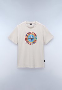 Camiseta de algodón color beige claro con un diseño de brújula redondeada y multicolor que presenta varias banderas nacionales y texto. Cuello redondo, mangas cortas.