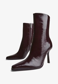 Burgundské členkové čižmy s lesklým povrchom, špicatou špičkou, vysokým stiletto podpätkom a bočným zipsom, ktoré predvádzajú elegantný siluetu.