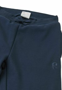 Granatowe spodnie dresowe z ryżowym pasem, regulowanym sznurkiem i małym wytłoczonym logiem na nogawce. Miękka tkanina, luźny krój.