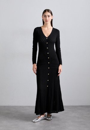 Black knit cardigan dress featuring a v-neck, long sleeves, diamond pattern, gold buttons, and a flared bottom. Material appears textured.