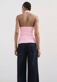 Pink halter top with a fitted bodice and open back, paired with navy wide-leg jeans featuring back pockets and contrast stitching.