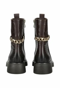 Ciemnobrązowe ankle boots w wzór krokodyla z masywnymi podeszwami i złotym łańcuchem z tyłu, widziane od tyłu.