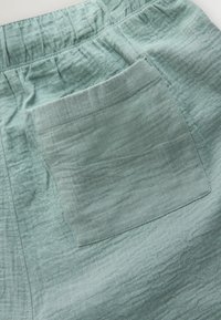 Pantalon en tissu vert clair froissé avec une ceinture élastique et une poche arrière rectangulaire cousue.