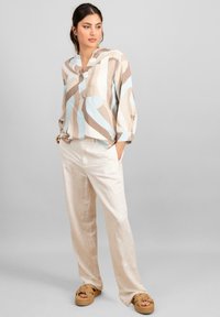 Top in lino con strisce astratte multicolori in beige, blu e marrone; abbinato a pantaloni larghi color crema e sandali platform intrecciati color tan.