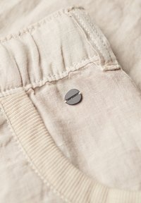 Tessuto beige chiaro con superficie texture, dotato di un elastico in vita e di una piccola etichetta metallica con la scritta 'SUPERDRY' cucita di lato.