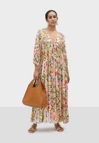 Färgglad maxiklänning med ett lagerdesign, som har livliga mönster i rosa, grön och gul. Kombinerad med en brun läderhandväska.