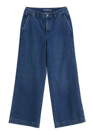 Tumed sinised laiad teksapüksid vööloopidega, esikottide ja nööpsulguriga, laotatud valgele taustale.