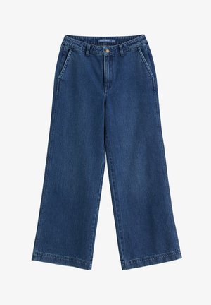 Tumed sinised laiad teksapüksid vööloopidega, esikottide ja nööpsulguriga, laotatud valgele taustale.