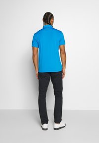 Blå kortärmad polo med rak skärning, i kombination med svarta byxor och vita sneakers. Slät textur, minimalistisk design.