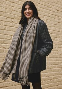 Navy striped coat with large buttons, worn over a black top. A brown and cream houndstooth scarf with fringed edges drapes over the coat.