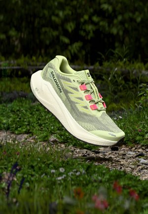 Chaussure de sport vert clair avec tige en mesh, accents roses et semelle texturée, présentant une forme profilée et un design de soutien.