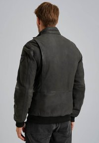 Giacca bomber in pelle nera con orlo a coste, dotata di colletto alto e toppe sulle spalle, che mostra una texture liscia e opaca.