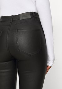 Zwarte neplederen hoge taille broek met twee achterzakken en een merklabel in de taille, met een elegante, gladde textuur.