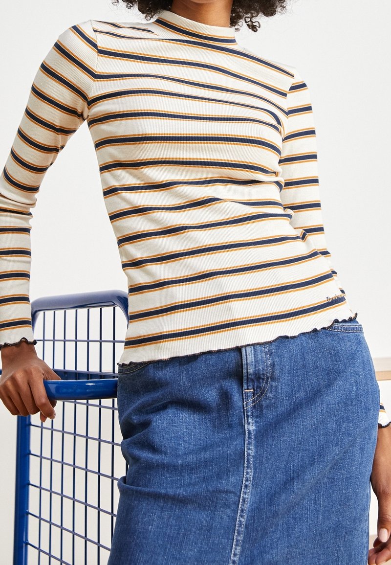 Gestreiftes Langarmshirt in Creme, Marineblau und Orange mit gerippter Textur, ausgestattet mit einem Stehkragen und gewelltem Saum. Kombiniert mit einem Jeansrock.