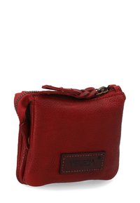 Rød læderpung med tekstureret overflade, lynlåslukning og en fletstrap. Har et markant logo mærke på forsiden. Kompakt design.
