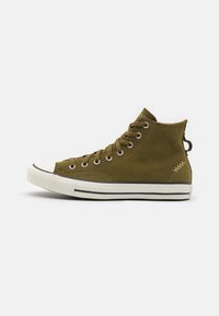 High-top sneakers in olive green suede with white rubber toe cap and sole, featuring metal eyelets and a loop at the heel.