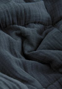 Dunkelgrauer, strukturierter Stoff mit sanften, zerknitterten Schichten und einem subtilen Webmuster, das ein lockeres und fließendes Erscheinungsbild vermittelt.