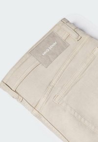Pantalones vaqueros de mezclilla beige con una textura suave, con una etiqueta rectangular cosida en la cinturilla que dice "MNG DENIM."