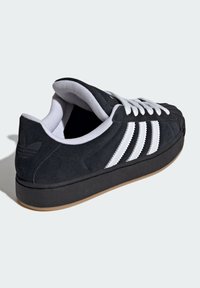 Čierna semišová teniska s bielym trojpásikovým zdobením, gumovou podrážkou, okrúhlou špičkou a látkovou podšívkou. Má polstrovaný lem a jazyk.