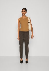 Tamni bez rukava top u kombinaciji s tamnosivim tapered jogger hlačama s vezicom i patentnim zatvaračima, završeno crnim cipelama na špic i krem torbom.