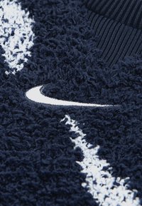 Tela polar azul marino con fibras texturizadas y peludas, con rayas blancas y un prominente logo Swoosh de Nike en blanco. Detalle de cuello acanalado.