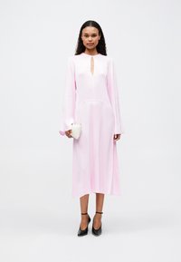 Langærmet, pink kjole med nøglehulsudskæring, en let tætsiddende talje og en flydende nederdel, parret med en lille tekstureret clutch og sorte hæle.