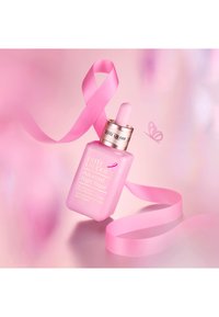 Flacon d'Estée Lauder Advanced Night Repair avec un ruban rose de sensibilisation au cancer du sein et un fond rose agrémenté de détails de papillon.