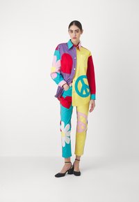 Colorful outfit featuring a button-up shirt with purple, red, and yellow sections, and pants with flower and peace symbol patterns.