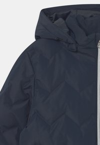 Veste rembourrée marine avec capuche, motif matelassé et zip argenté. Le tissu semble lisse avec une finition légèrement brillante.