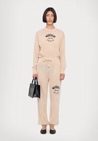 Bežna lounge postavitev z dolgimi rokavi in elastičnimi manšetami, ki vključuje črn logotip "Moschino Jeans". v kompletu z majhno črno torbico in ravnimi čevlji.