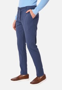 Pantaloni blu navy su misura con una texture liscia, dotati di vita con cordoncino e tasche laterali, abbinati a calzature marroni.