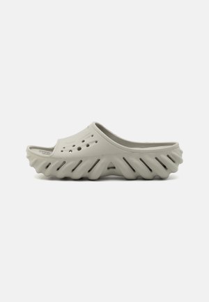 Light gray clogs with a cut-out design, featuring circular holes, textured side ridges, and an open back for easy slipping on.