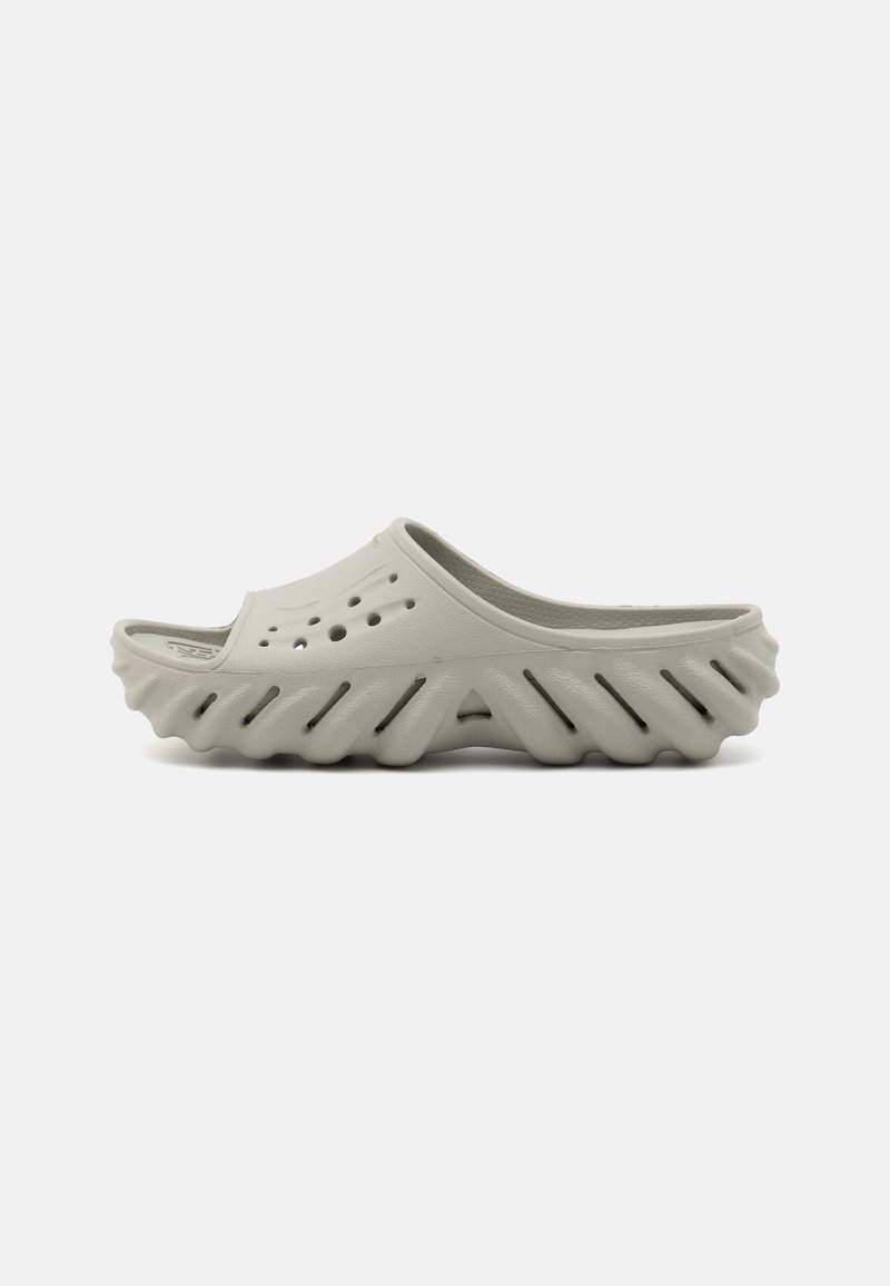 Light gray clogs with a cut-out design, featuring circular holes, textured side ridges, and an open back for easy slipping on.