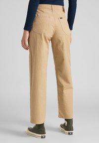 Ljusbeige kordbyxor med rak passform, med bakfickor och en läderetikett. Bärs med gröna högstövel sneakers.