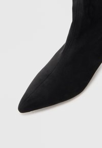 Stivale alla caviglia in suede nero con punta affilata e texture liscia, caratterizzato da un design senza cuciture e senza hardware o accenti visibili.