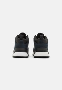Men's sneakers with a navy blue and black upper, padded collar, sturdy sole, and white midsole. Features textured materials and stitching details.
