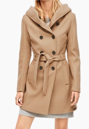 Femme portant un manteau en laine beige mi-longueur avec des boutons croisés et une ceinture nouée à la taille.