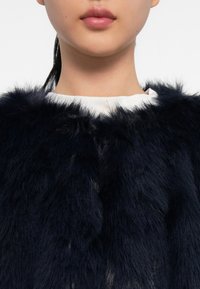 Collo in pelliccia sintetica blu navy con superficie morbida e testurizzata, che incornicia un collo bianco. Labbra e pelle lisce sono visibili sotto il collo.